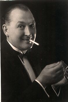 Studio portrait of Billy Matchett in evening dress, cigarette in mouth, grinning